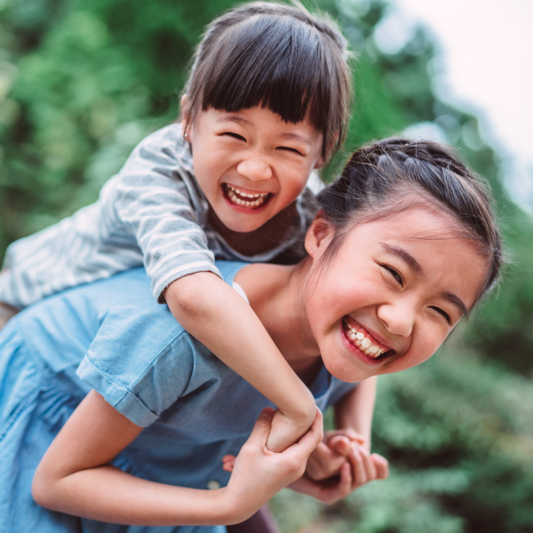 two girls laughing, younger girl on older girls back