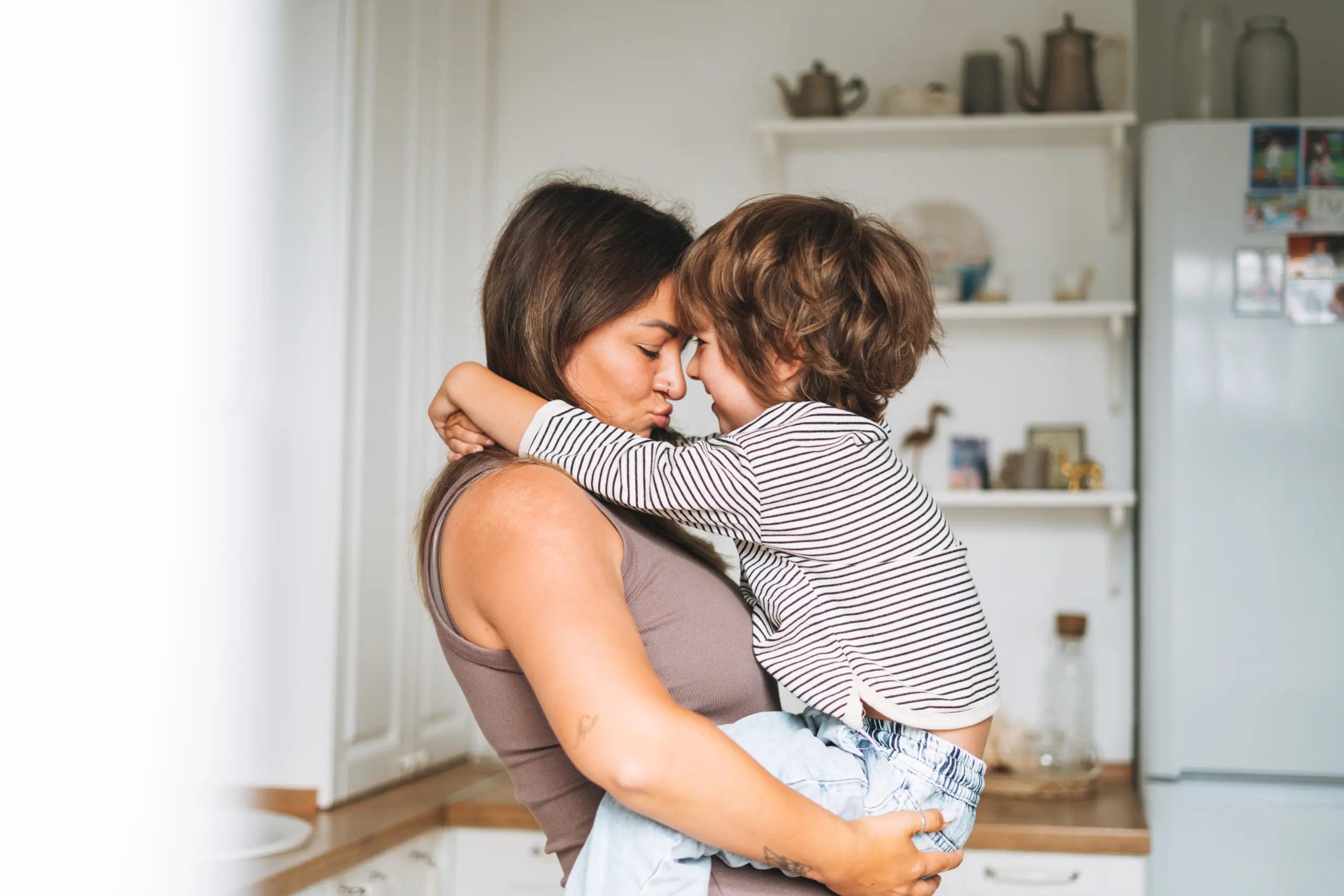Pregnant woman huging her son boy in arms in kitchen at home Programs & Services